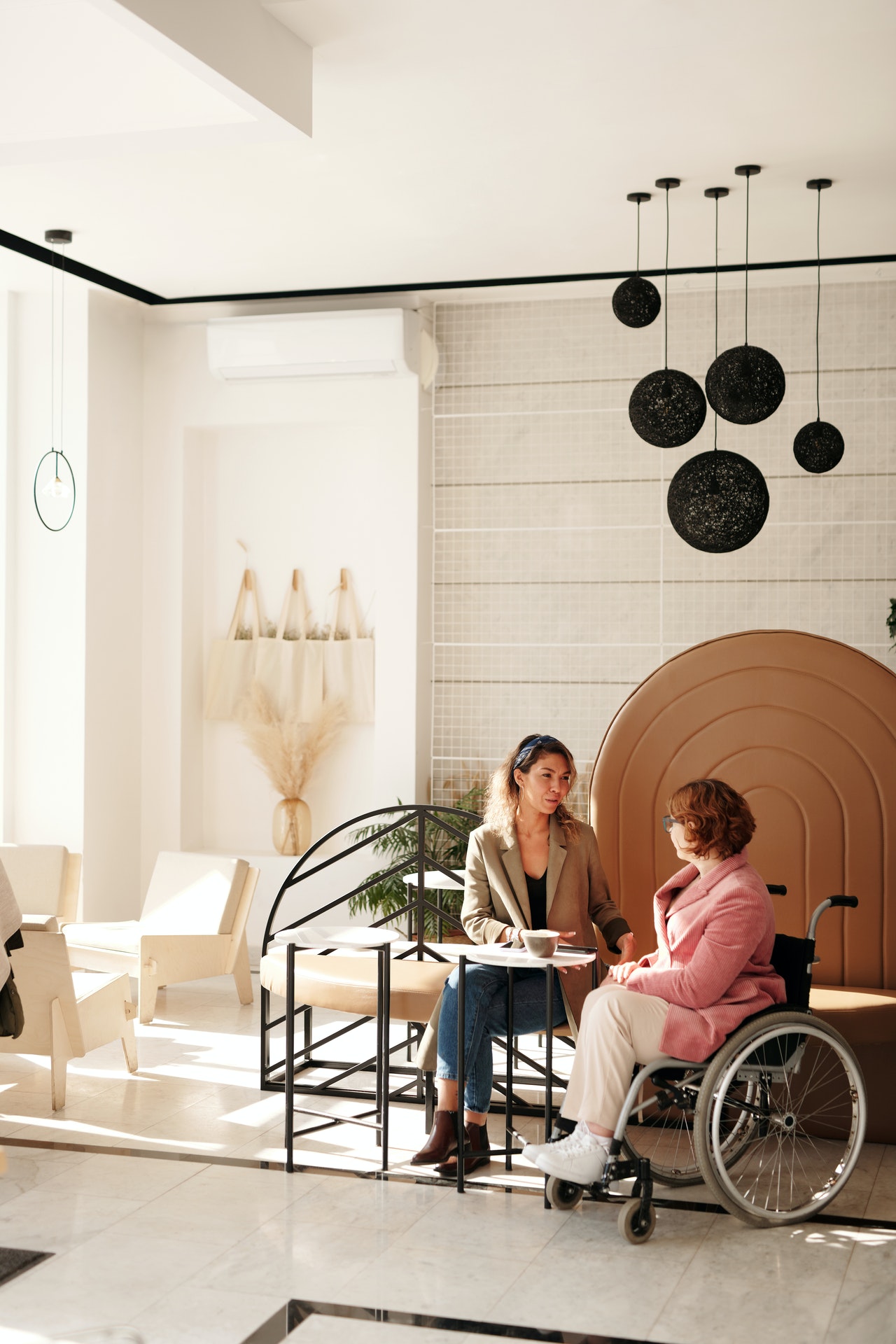 Žena za stolíkom a žena na invalidnom vozíku sa spolu rozprávajú