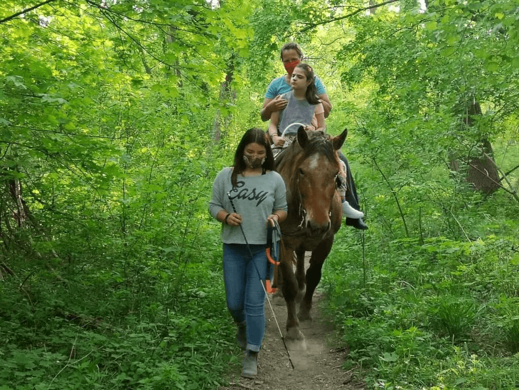 Žena vedúca koňa, na ktorom sedí žena s dievčaťom