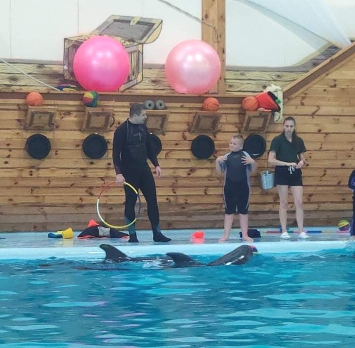 Delfínoterapia - na kraji bazéna stojí dospelý muž aj so ženou, muž sa rozpráva s chlapcom