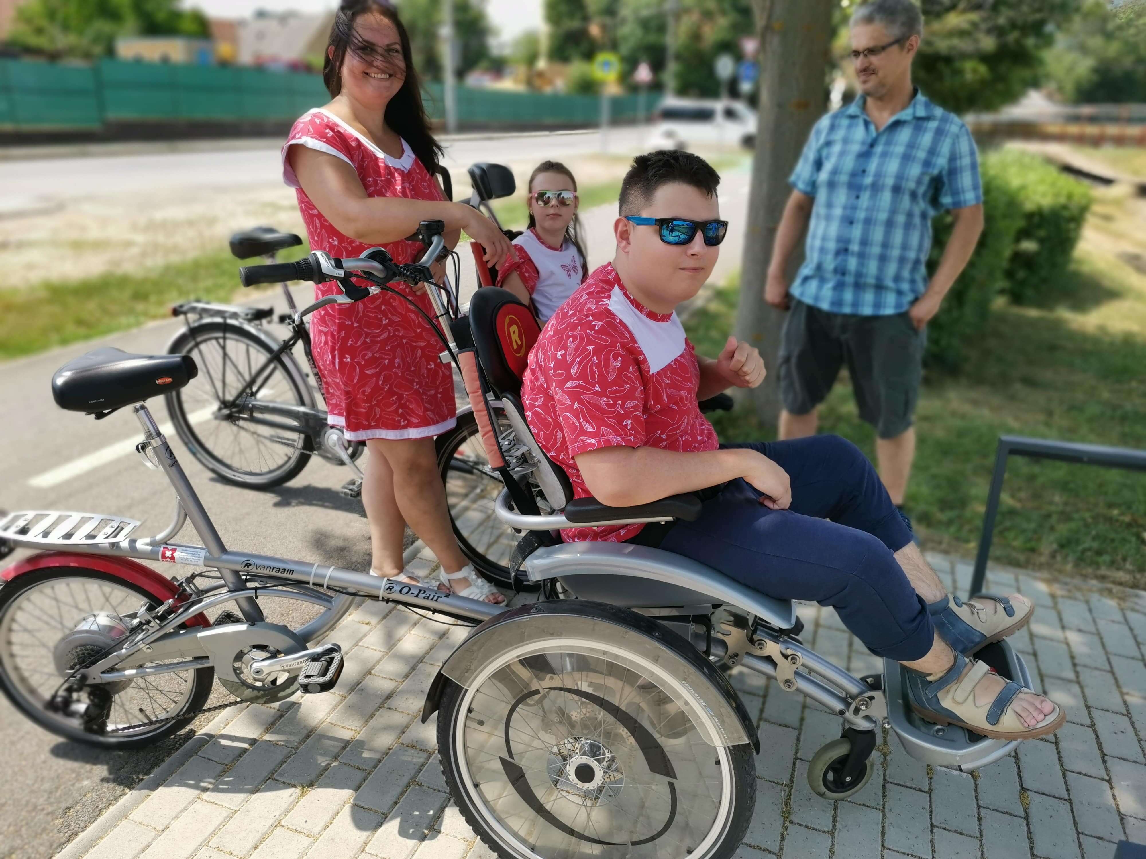 Chlapec na vozíku, ktorý je pripevnený na bicykli a zvyšok rodiny - otec, mama, sestra